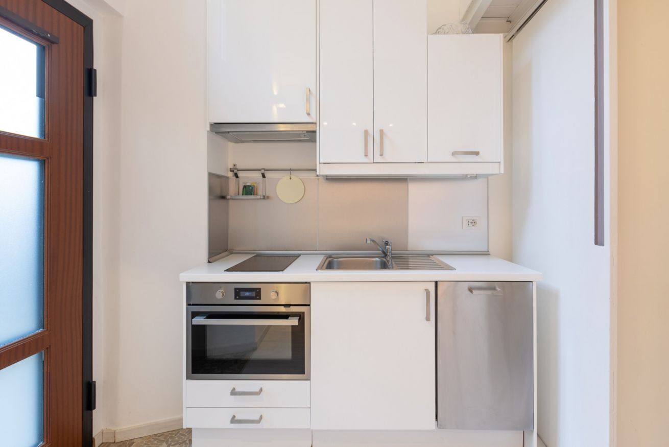 A compact kitchen with white cabinets, a stainless steel sink, and a built-in oven.