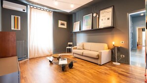 A modern living room with a sofa, coffee table, and floor lamp. There are framed pictures on the wall and a radiator on the left. - Bright and spacious one-bedroom apartment of almost 100 square meters located in Via Carlo d'Adda 5, in the heart of Milan, in an IN area full of life and with numerous connections via local transportation (P.ta Genova FS station and metro stop a few min (Milano)