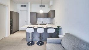 A modern kitchen with a central island, bar stools, and a grey sofa in a living area. - Two-room apartment Cecchi 18 2p - Mirable PM (Milano)