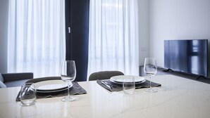 A dining table set with plates, glasses, and cutlery in a modern room with a large window and a flat-screen TV. - Two-room apartment Cecchi 18 2p - Mirable PM (Milano)