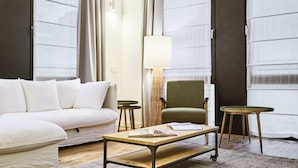 Et moderne hotelværelse med en hvid sofa, et træsofabord, en grøn lænestol og et lille rundt bord.