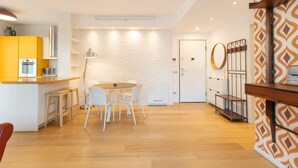 Une cuisine moderne avec des meubles blancs, un coin repas doté d’une table ronde et de chaises, et un mur orné d’un motif sur le côté droit.