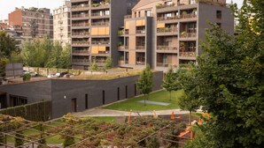 Un immeuble d’appartements moderne doté de nombreux balcons, d’un jardin sur le toit et d’une cour intérieure avec des arbres et un espace de jeux pour enfants.