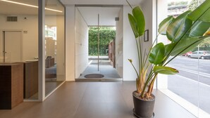 Un espace d’accueil avec une cloison en verre, un comptoir de réception, une plante en pot et une vue sur la rue.