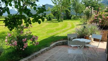Eine Terrasse mit Steinfliesen, weißen Metallstühlen und einem Tisch.