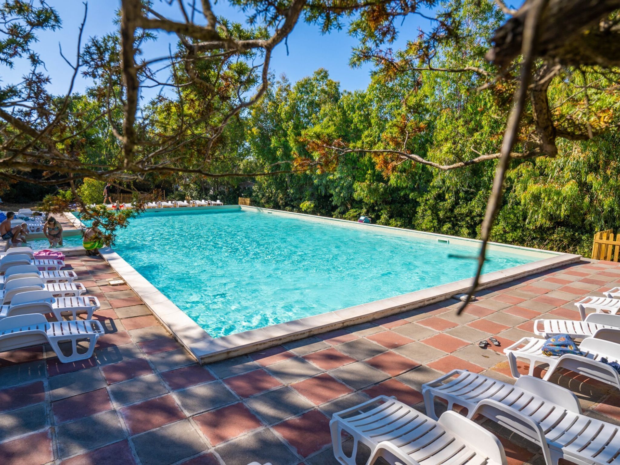 Une piscine rectangulaire à l’eau d’un bleu limpide, entourée d’une terrasse carrelée où sont disposées des chaises longues blanches.