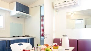 A compact kitchenette with a gas stove, a coffee maker, and a dining table set with cups, a bowl of cherries, and a bowl of grapes.