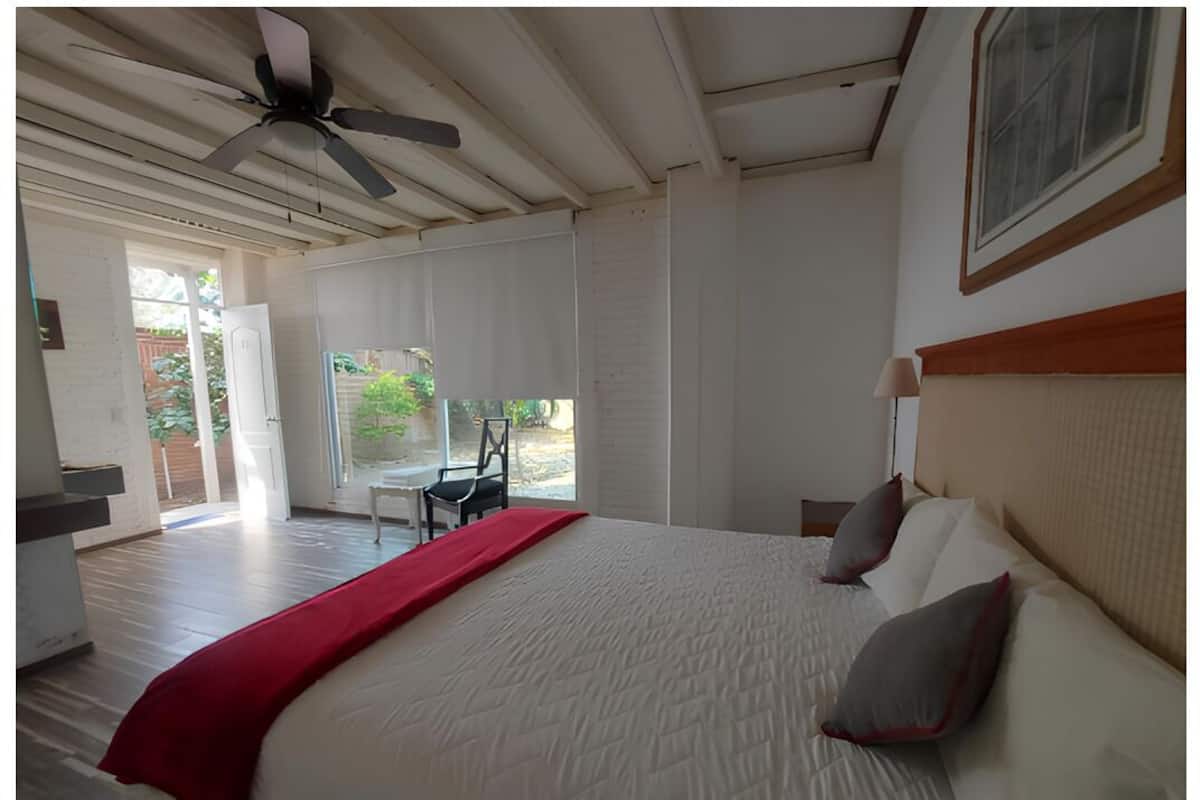 A bedroom with a large bed, a ceiling fan, and a view of the outdoors.