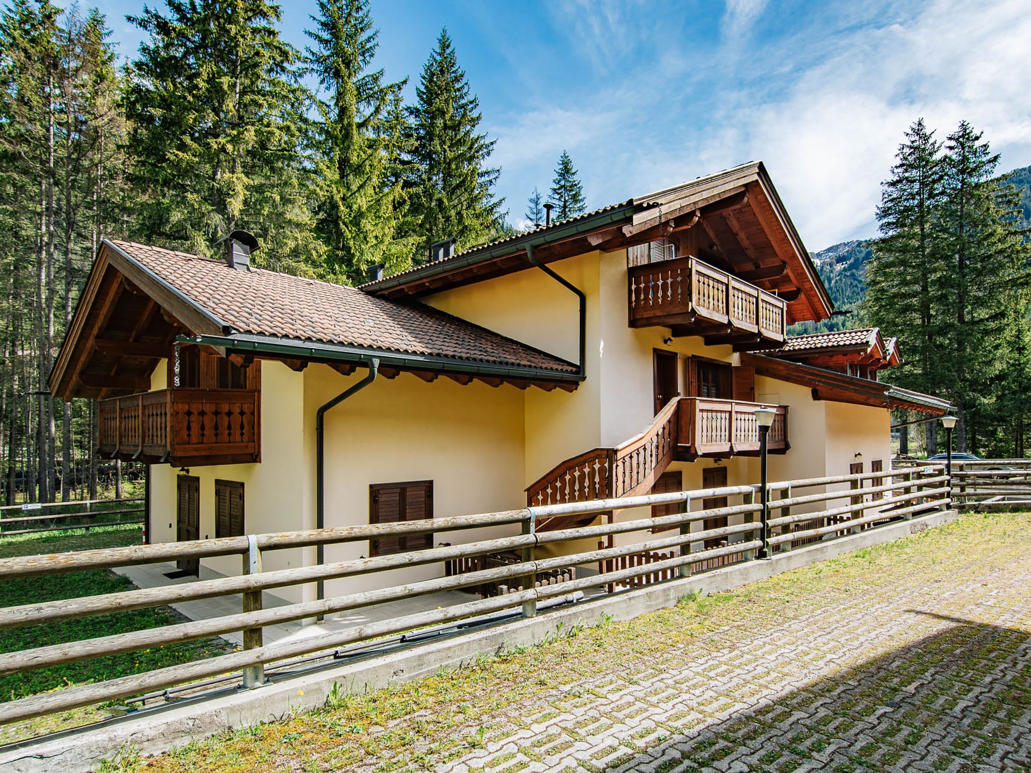 A traditional chalet with a wooden balcony, a stone staircase, and a view of the surrounding forest.