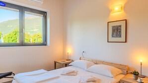 A neatly made bed with white linens and towels, a bedside table with a lamp, and a framed picture on the wall.