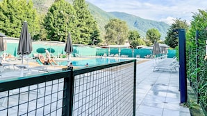 A pool area with lounge chairs and umbrellas, surrounded by greenery and mountains.