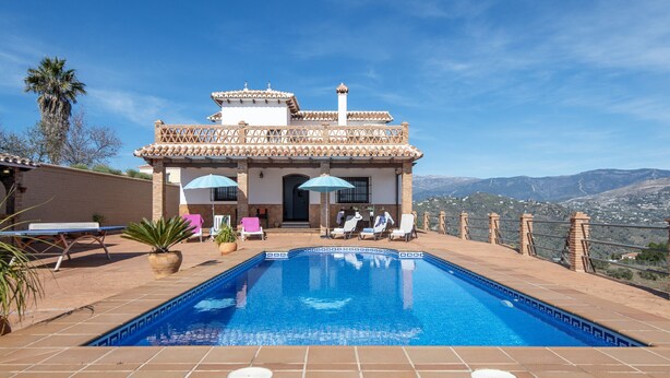 A pool area with a view of mountains, a patio with lounge chairs, and a building with a tiled roof. - Casa Ascen by At Home Costa del Sol (Torrox)