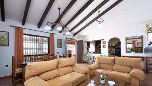 A spacious living room with two beige sofas, a wooden coffee table, and a dining area with a wooden table and chairs. - Casa Ascen by At Home Costa del Sol (Torrox)