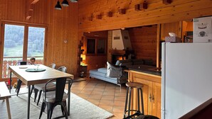En stuga med träpanel på insidan, innehållande en matplats, ett kök och en öppen spis.