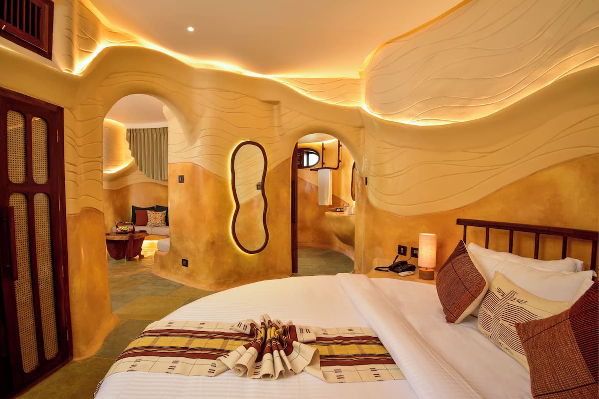 A uniquely designed bedroom with curved walls, a large bed, and a nightstand with a lamp.