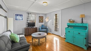 Una sala de estar con un sofá gris, un aparador verde azulado, un sillón azul, una mesa de centro de madera y un televisor sobre un mueble.