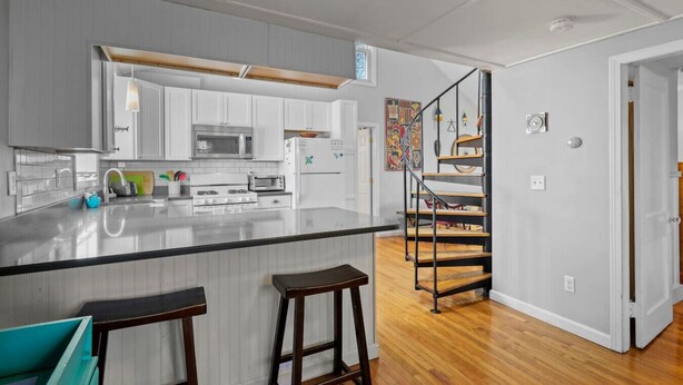 Una cocina moderna con armarios blancos, una isla central con taburetes, una estufa de acero inoxidable y una escalera de madera.