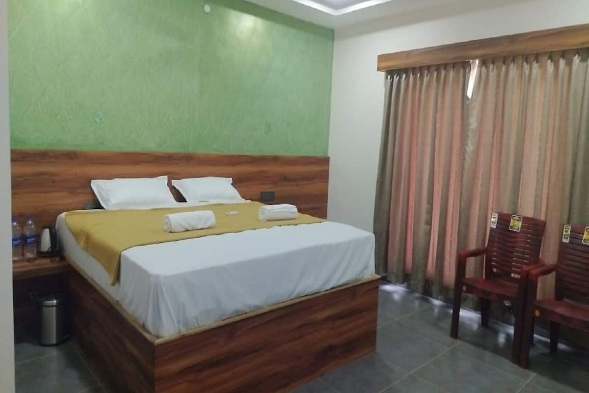 Une chambre d’hôtel avec un lit en bois, une table de chevet avec une lampe, une poubelle et une fenêtre avec des rideaux.