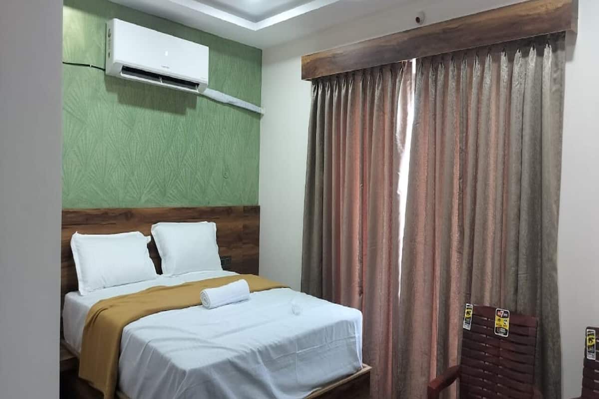 Une chambre d’hôtel avec un lit, un mur texturé de couleur verte, un appareil de climatisation et une fenêtre avec des rideaux.