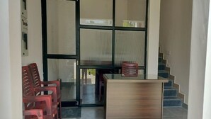 A reception area with a wooden desk, red plastic chairs, and a staircase in the background. - Trigon Retreat (Puducherry)