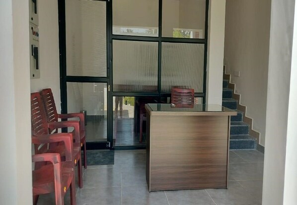 Un área de recepción con un escritorio de madera, sillas de plástico rojas y una escalera al fondo.