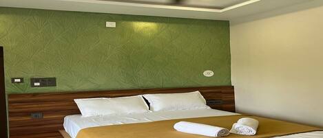 Una habitación de hotel con una cama, un ventilador de techo, una pared verde con textura y un cabecero de madera.