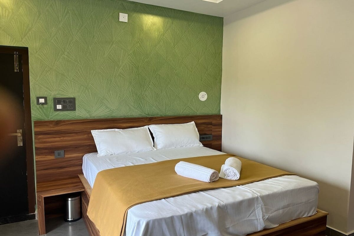 Une chambre d’hôtel avec un lit, une tête de lit en bois, un mur d’accent vert et une petite poubelle.