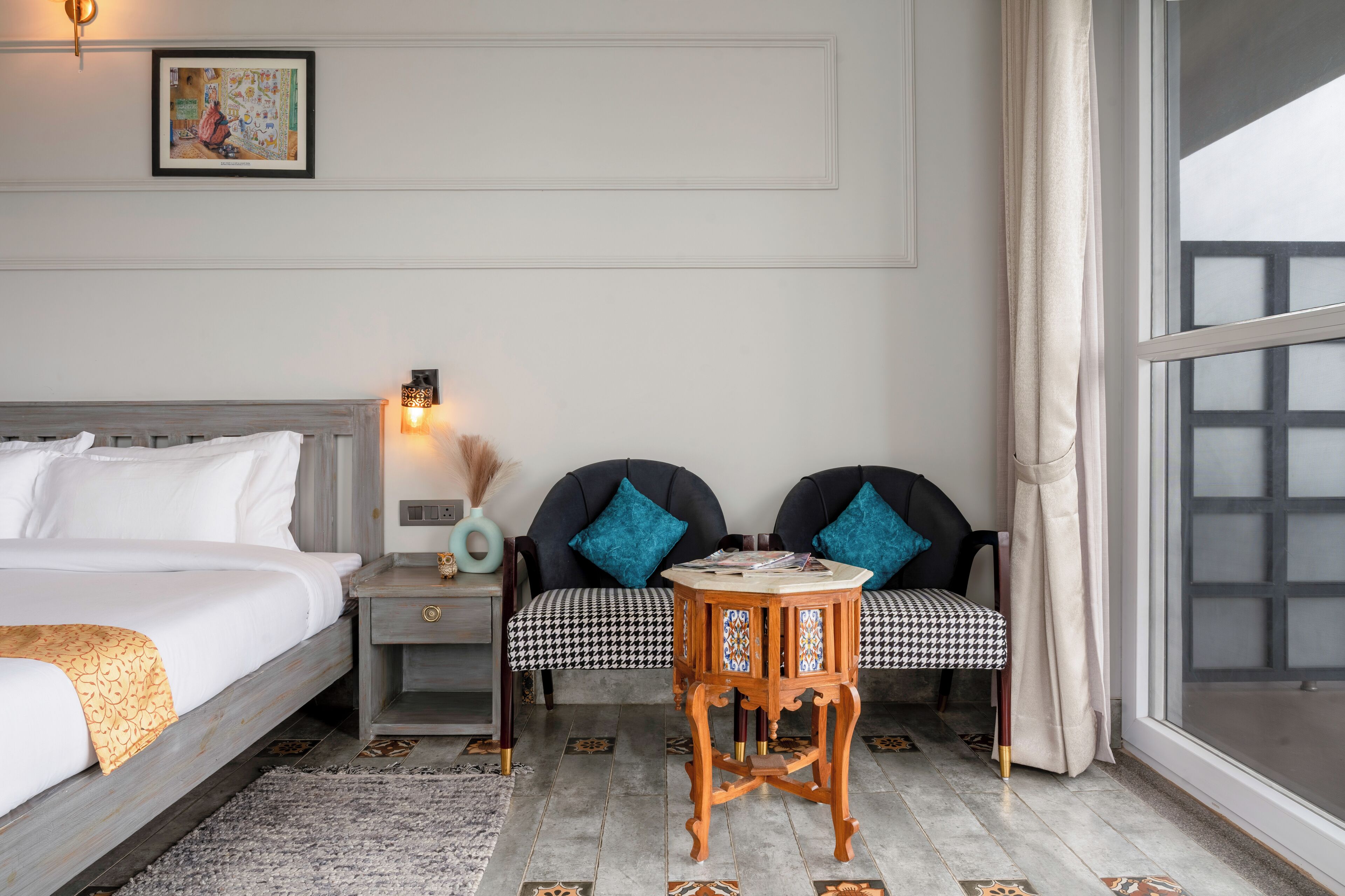 A hotel room with a bed, two armchairs, a small table, a nightstand, and a large window.