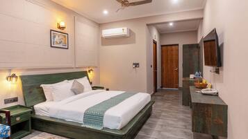 Habitación de hotel con cama, escritorio, ventilador de techo, aire acondicionado y televisor.