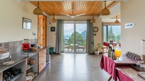 A spacious kitchen with a view to the outdoors, a dining area with a table and chairs, and a sign indicating the location of the bathroom. - Yecha House - Mountain & Lake View Retreat, Bhimtal (Bhimtal)