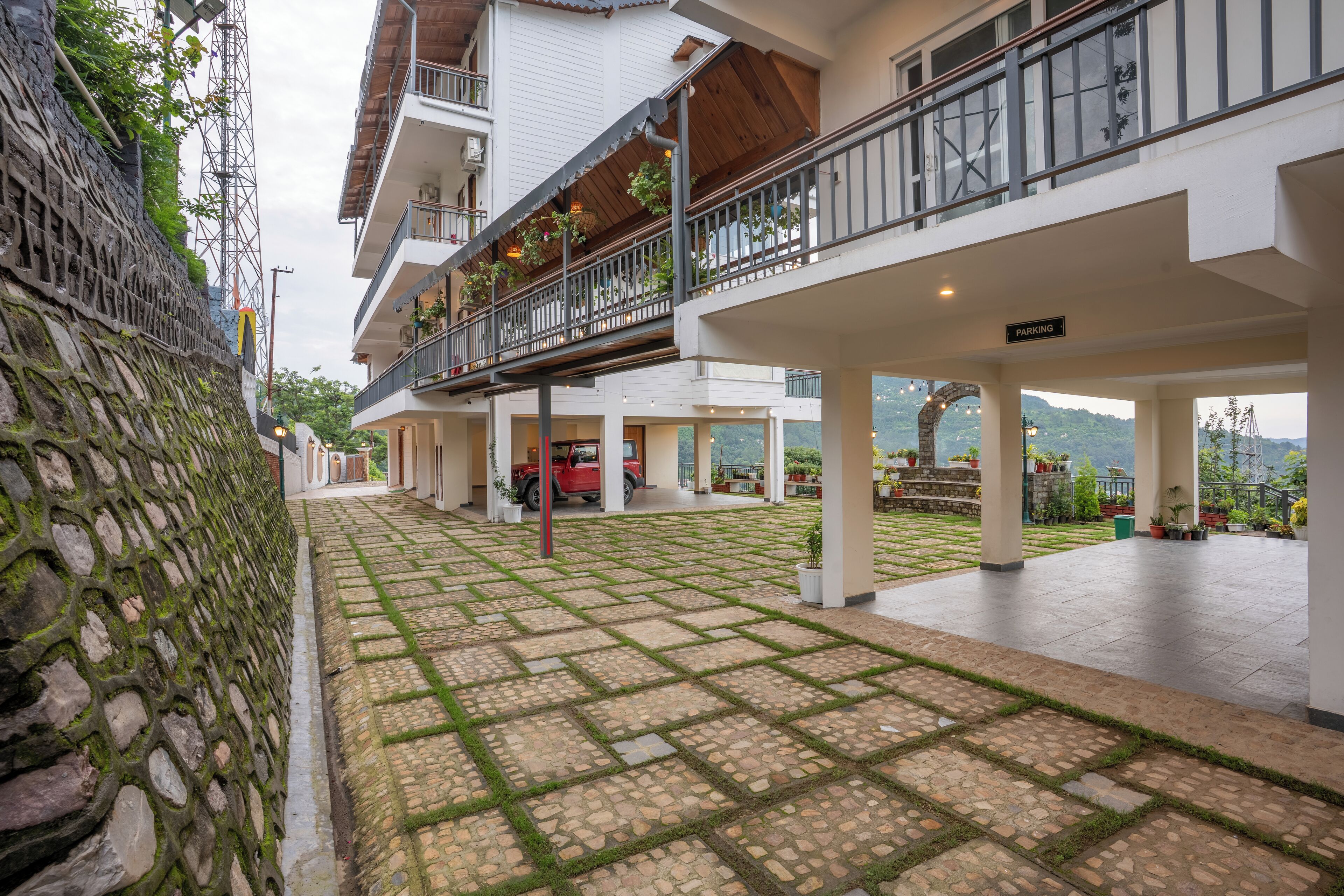 A hotel courtyard with stone flooring, potted plants, and a red vehicle parked inside.