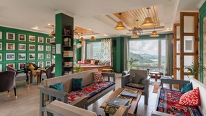 A spacious living area with multiple seating options, a bookshelf, and large windows offering a view of the outdoors. - Yecha House - Mountain & Lake View Retreat, Bhimtal (Bhimtal)