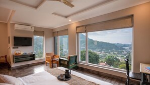 A spacious bedroom with a large bed, a desk, and a view of a mountainous landscape through large windows. - Yecha House - Mountain & Lake View Retreat, Bhimtal (Bhimtal)