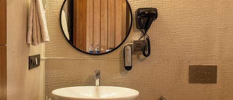 A bathroom with a white sink, a round mirror, a hairdryer, and a toilet.