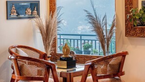 A dining area with two wooden chairs and a table, a large window with a view, and wall-mounted decorative items. - Yecha House - Mountain & Lake View Retreat, Bhimtal (Bhimtal)