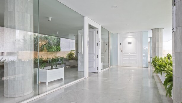 Een moderne hal met glazen wanden, een witte bank en potplanten.