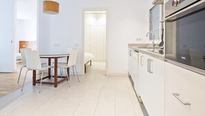 Een moderne keuken met witte kasten, een inbouwoven en een eethoek met een glazen tafel en stoelen.