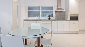 Een moderne keuken met witte kastjes, een granieten aanrechtblad, een inbouwoven en een glazen eettafel met stoelen.