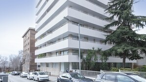 Een meerlaags gebouw met een modern architectonisch ontwerp, voorzien van balkons en een parkeerplaats met meerdere auto's.