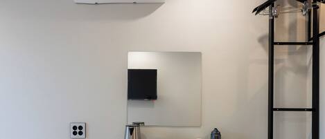 A compact hotel room with a bed, a desk with a computer, a small fridge, and a wall-mounted air conditioner.