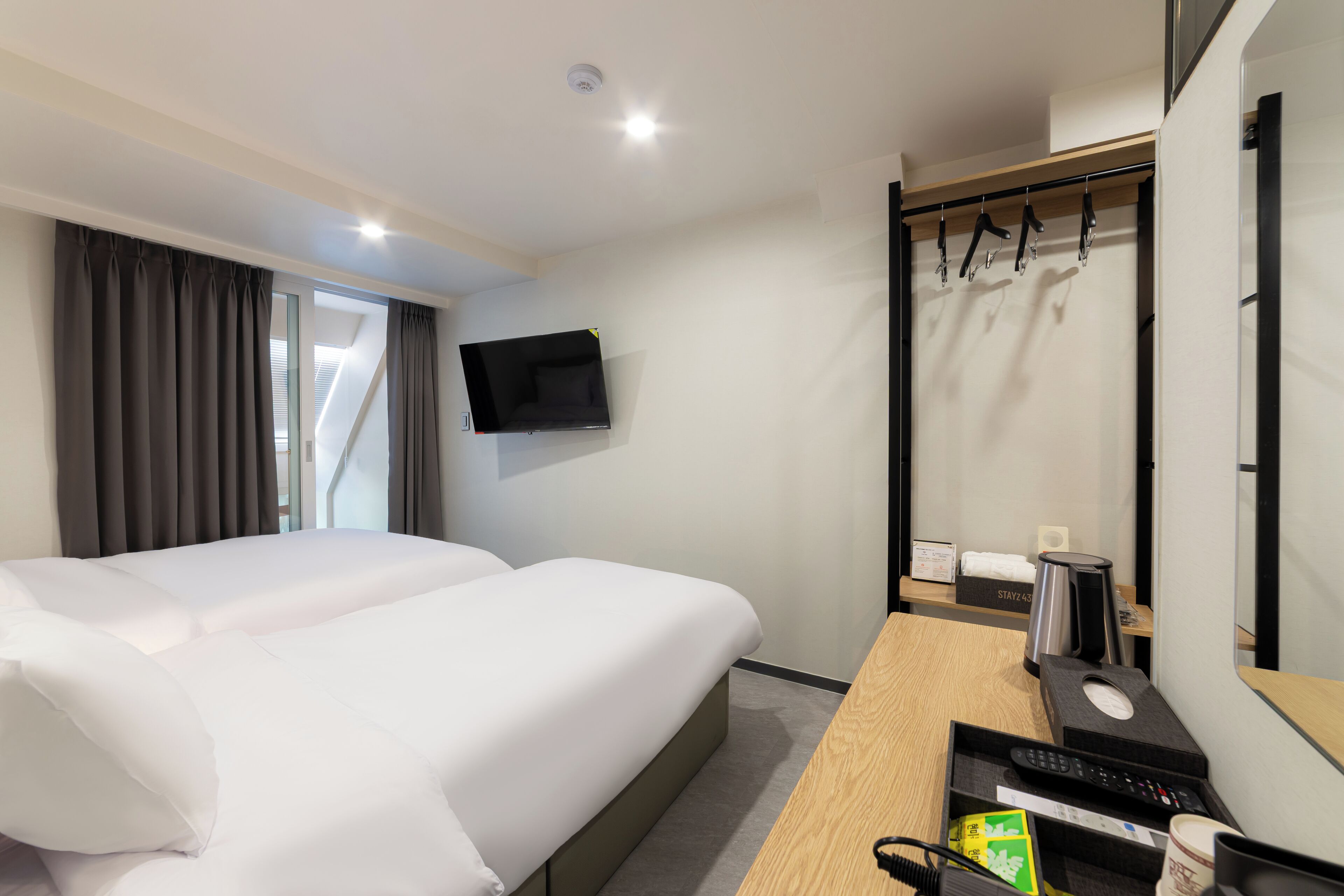 A hotel room with a bed, a desk with a computer, a coffee maker, and a TV mounted on the wall.