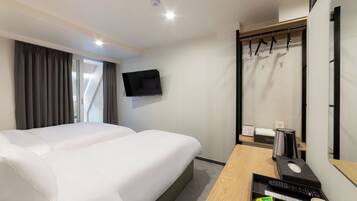 A hotel room with a bed, a desk with a computer, a coffee maker, and a TV mounted on the wall.