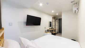 Une chambre d’hôtel équipée d’un lit, d’un bureau, d’un téléviseur à écran plat fixé au mur et d’un petit coin cuisine.