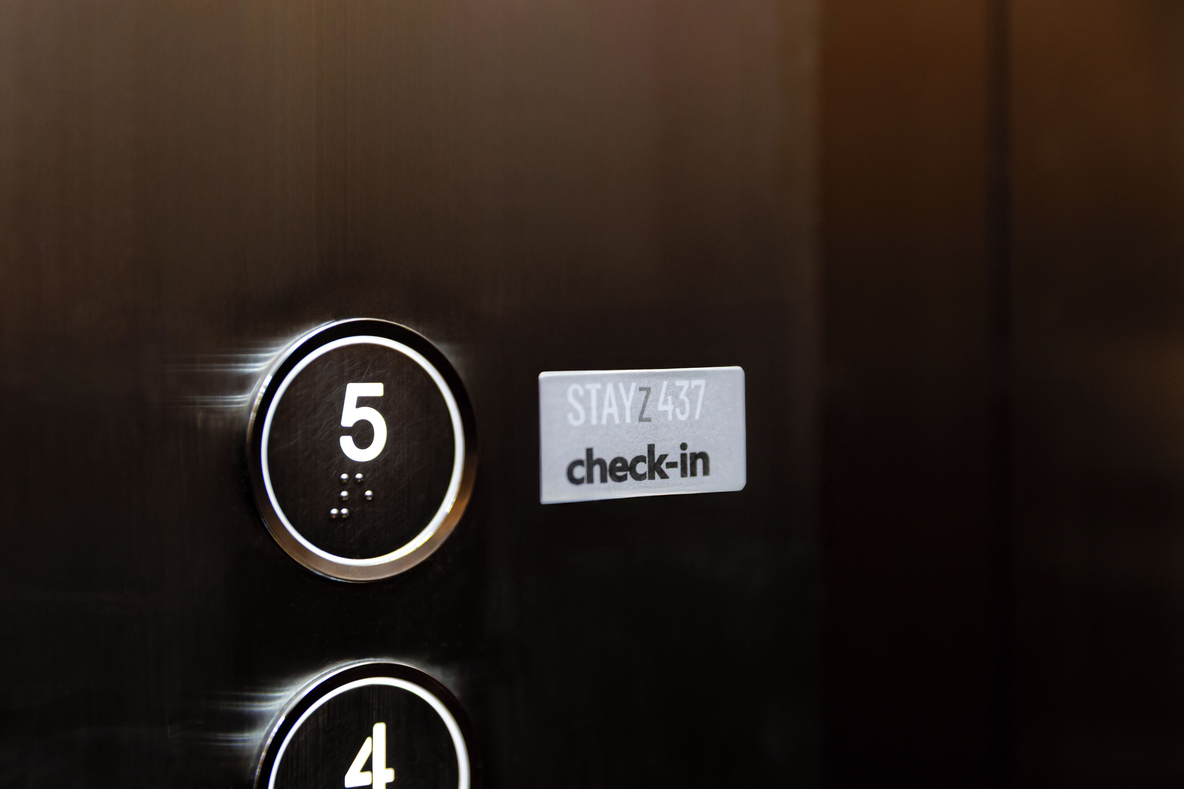 An elevator control panel with buttons labeled 5 and 4, and a sign that reads "STAY 437 check-in".