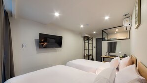 Ett hotellrum med två sängar, en tv som är monterad på väggen, en spegel och ett litet bord med en vattenkokare.