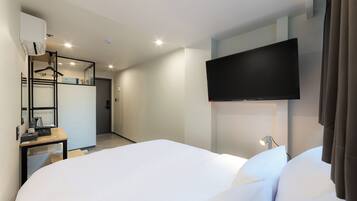 Et moderne hotelværelse med en stor seng, et fladskærms-tv monteret på væggen, et skrivebord med lampe og et garderobeskab med spejl.