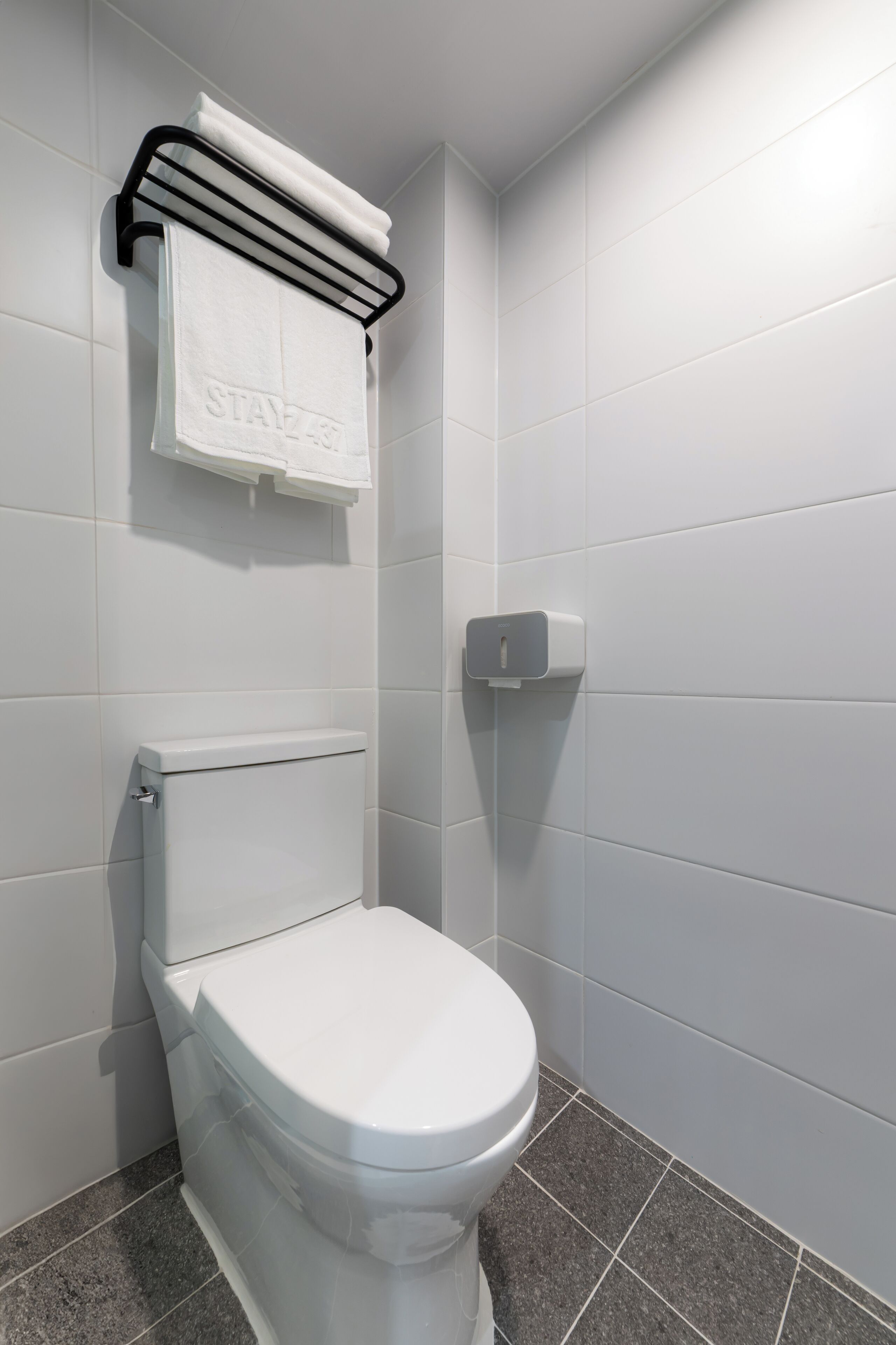 A modern bathroom with a white toilet, a towel rack, and a soap dispenser.