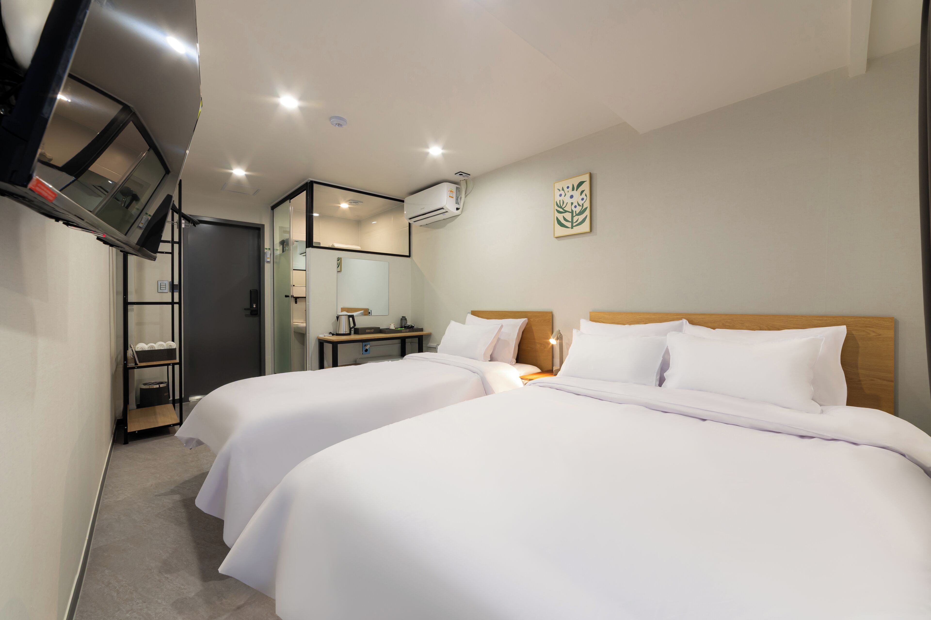 A hotel room with two beds, a desk, a chair, a TV mounted on the wall, and an air conditioning unit.