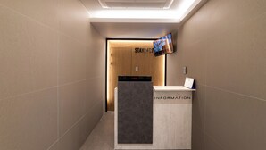 Ett receptionsområde med en receptionsdisk märkt med texten ”INFORMATION”, en väggmonterad TV och en trädörr med skylten ”STAYZ 437”.