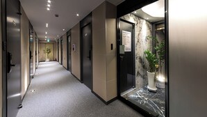 En modern hotellkorridor med en vägg av marmor, krukväxter och en hiss.